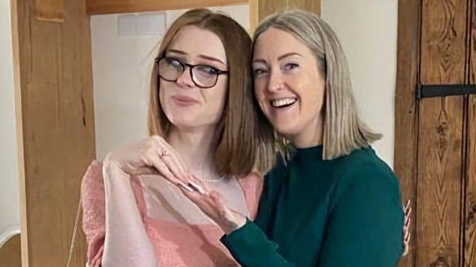 Brianna Ghey, with straight reddish-brown hair and wearing a pink top and glasses, poses with her mother Esthey Ghey, who has shoulder length blonde hair and is wearing a green jumper. 