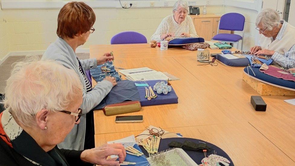 Ladies sat at a table making lace