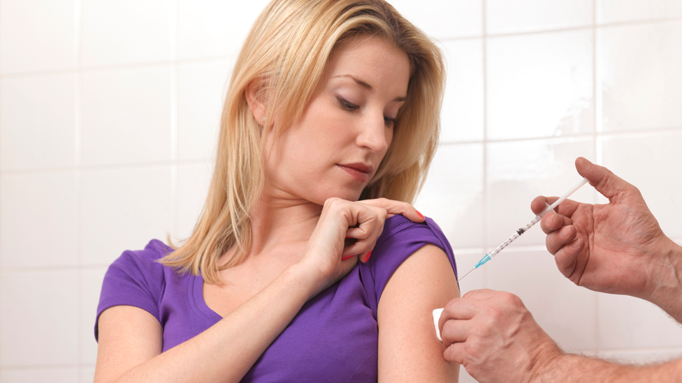 Woman receives flu vaccine jab in the top of her arm