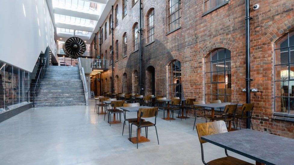 Ground floor of Derby Museum of Making showing a seating area with wooden chairs, grey floor and brick walls