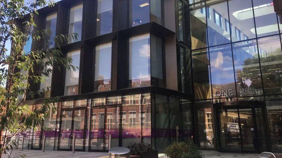 West Northamptonshire Council headquarters. On the right third is the glazed entry with the entrance on the ground floor and through the two storeys of glass a glimpse of an atrium rising to windows in the roof. On the left, two thirds are black framed windows