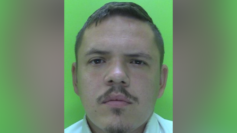 A police mugshot of a man with a goatee beard and moustache