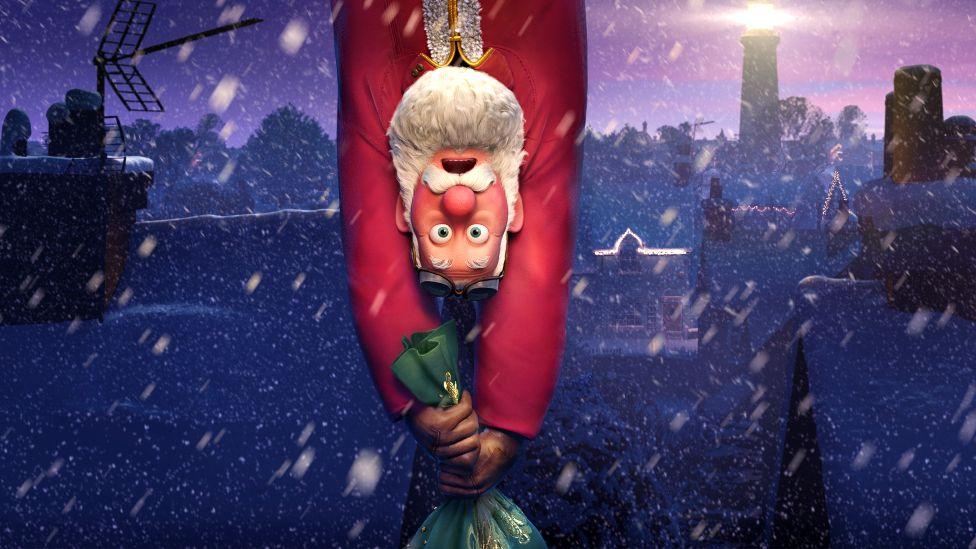 Santa Claus hanging upside down, clinging on to his sackful of presents as they dangle beneath him, in a promotional still for Netflix's That Christmas