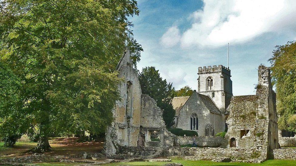 Ruins of walls with masonry scattered on grounds and tower seen behind