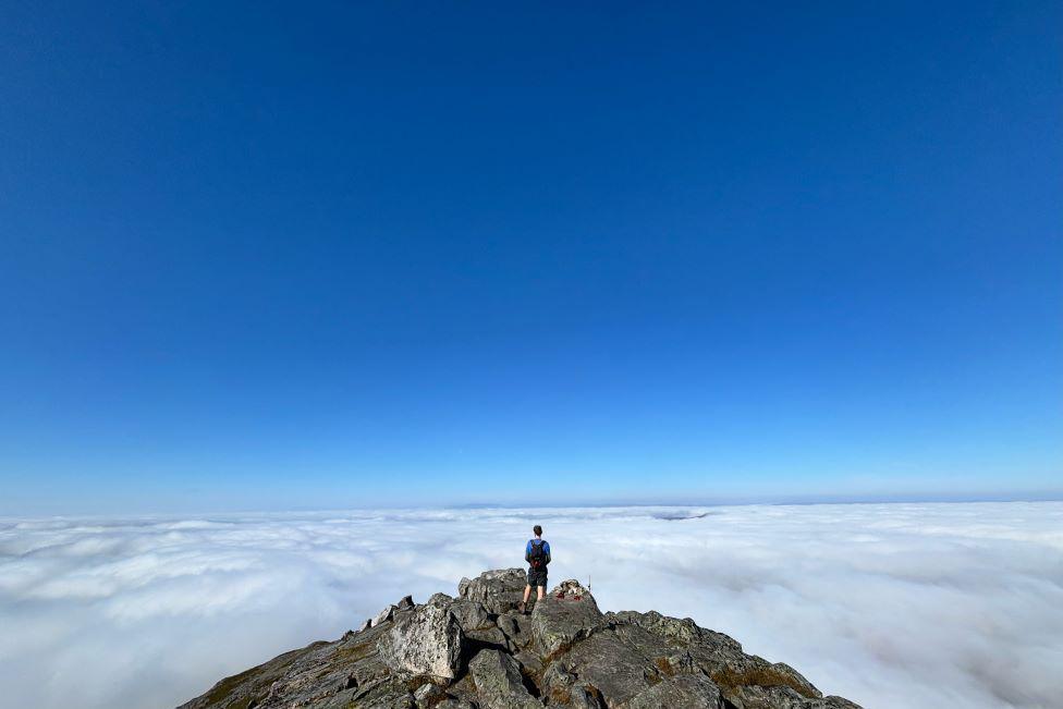 Man at peak of Schiehallion, above clouds, with blue sky in background