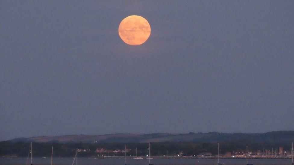 Boats on the water with rolling hills behind and the supermoon above