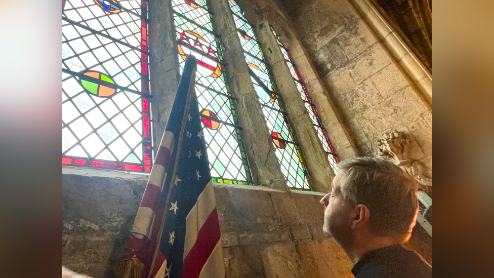 A vicar looks up at a stained glass window inside the abbey. An American flag has been installed in front of it.