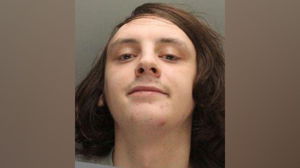 Police image of James Foy, who has long brown hair and a grey sweatshirt on