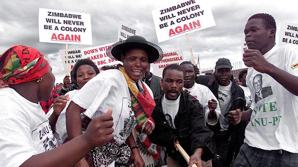 A crowd Zanu-PF supporters dance together as they welcome President Robert Mugabe home from a trip abroad in 2000, with placards saying ‘Zimbabwe will never be a colony again’.