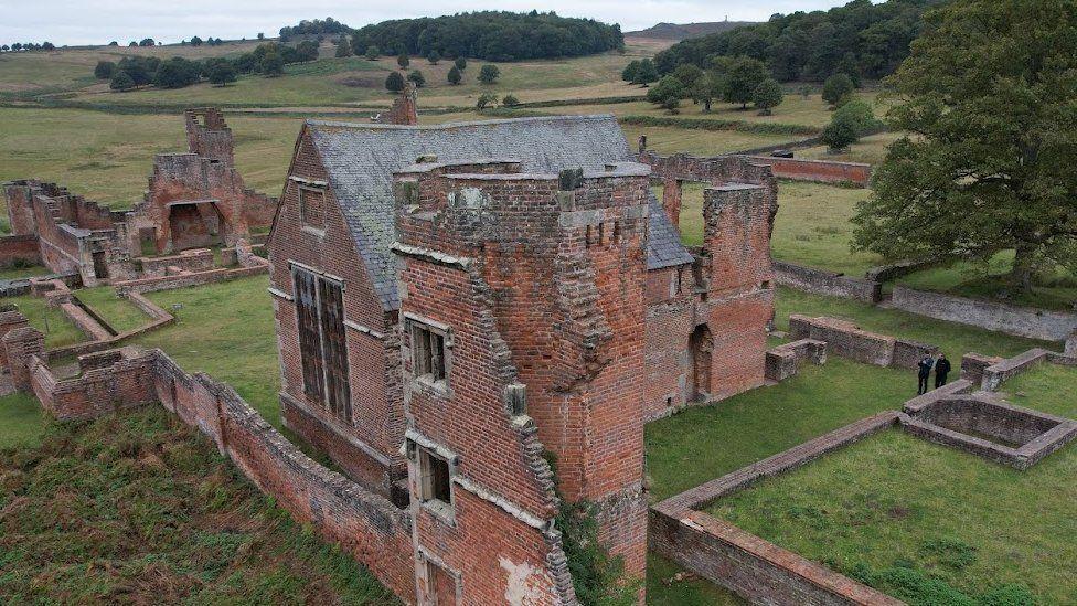 The Bradgate House ruins and Chapel, a red brick building, with half walls around the edges and green lawns in Bradgate Park, Leicestershire