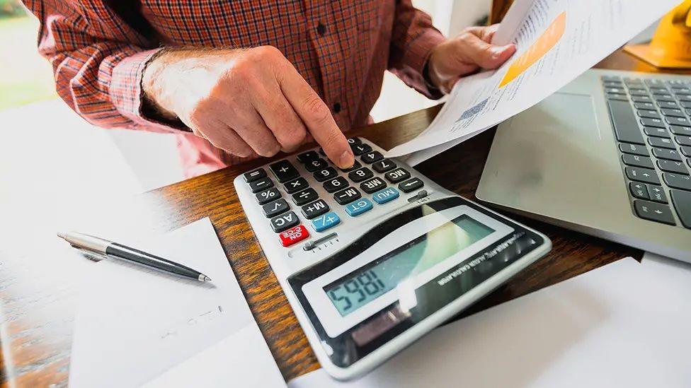 Man with bills sits working out his accounts using a calculator 