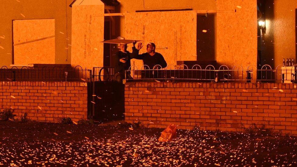 Two men take shelter from embers blowing from a bonfire at Hopewell Square in Belfast's Shankill area