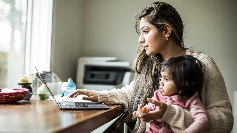 Mother multi-tasking with infant daughter in home office