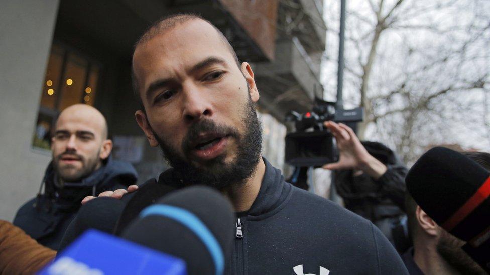 Influencer Andrew Tate speaks to the media while being escorted by police officers