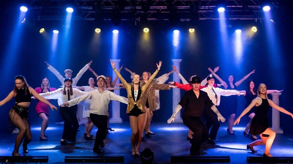 A group of young people on stage in theatrical costumes