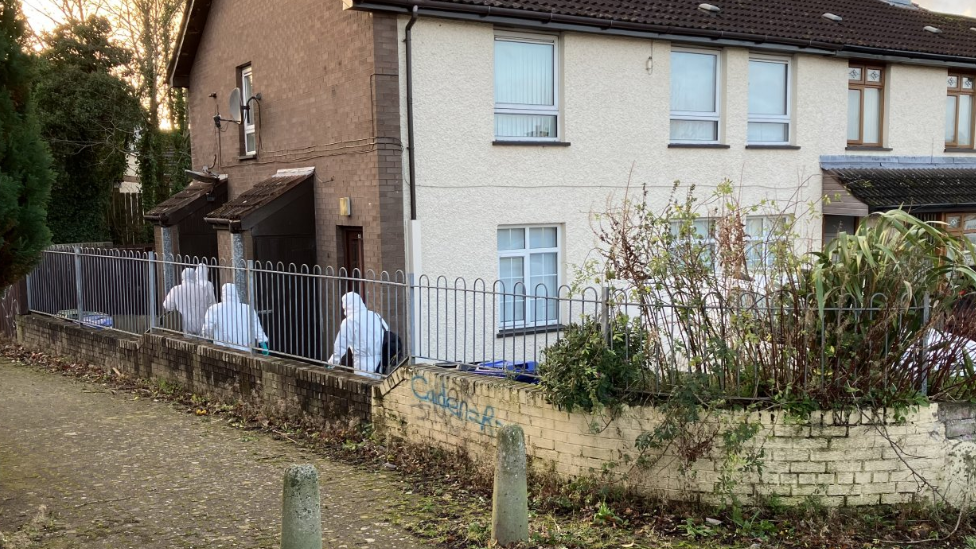 Shows four poeple in white forensics suits arriving at a house 