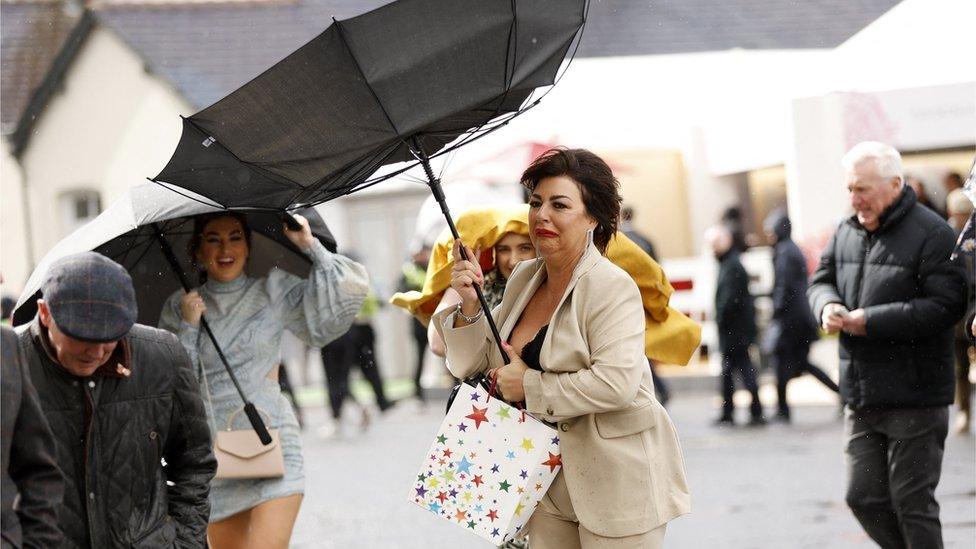 Woman tries to keep hold of umbrella in windy conditions at Aintree