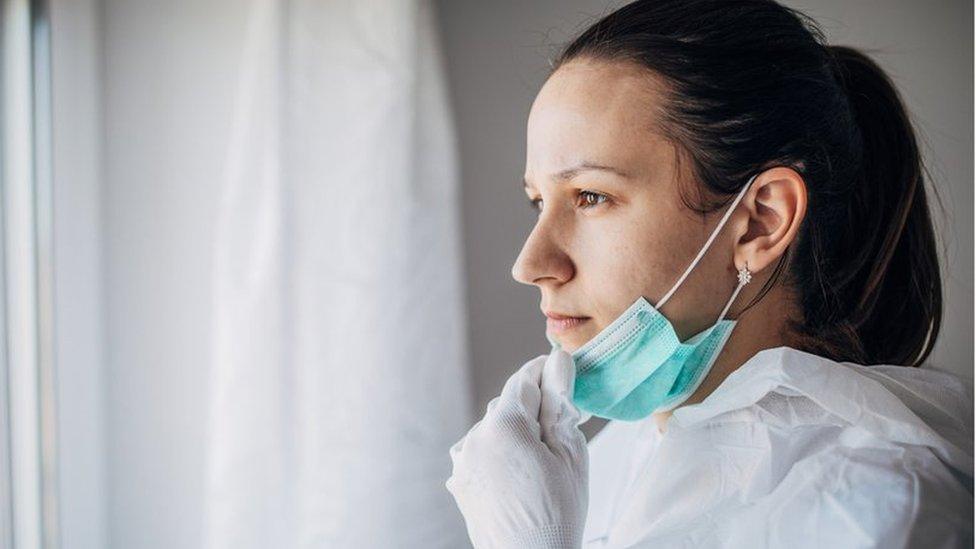 A concerned doctor in PPE looking out of a window