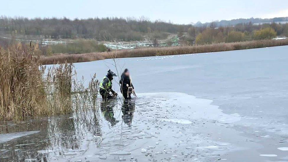 A police officer in off road bike gear rescuing a woman and her dog from a frozen lake