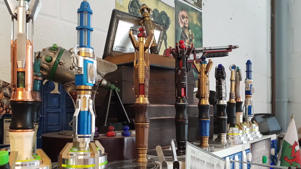 Photo of a shelf full of sonic screwdrivers and other props