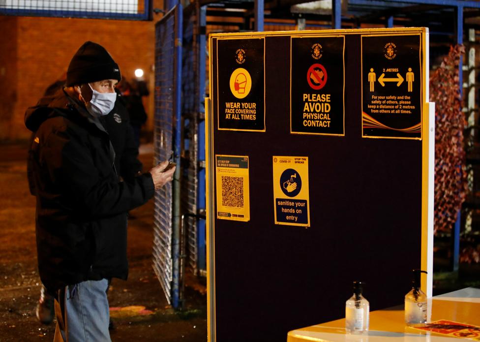 A Luton Town fan wearing a protective face mask stands outside the stadium before the match