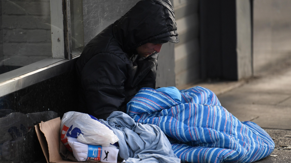 Someone sits on the street covered in a blanket