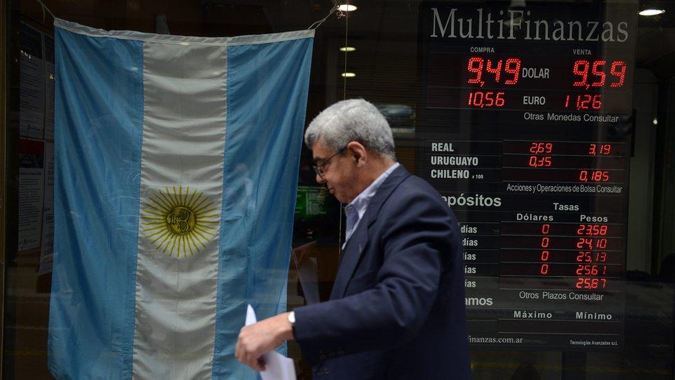 A man walks by a foreign exchange bureau with an Argentine flag hanging in the window