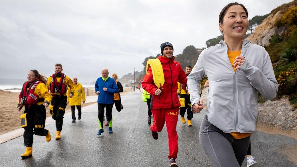 People running near the sea edge - a woman at the front is wearing a RNLI Lifeboats top