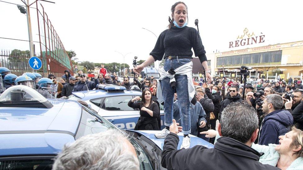 Relatives of inmates protest as law enforcement officers stand outside the Rebibbia prison in Rome, where a riot earlier broke out, 9 March 2020