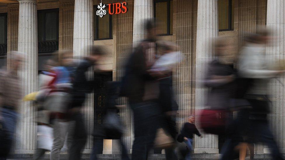 Commuters walk past the entrance of a branch of Switzerland's largest bank UBS in Lausanne