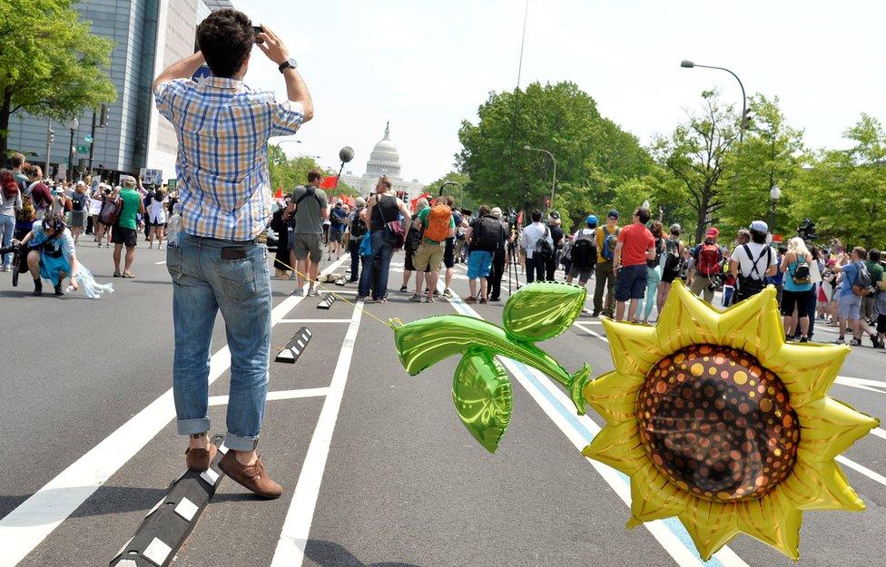 A man with a giant balloon of a sunflower tethered to himself waits for the start of a march by demonstrators down Pennsylvania Avenue