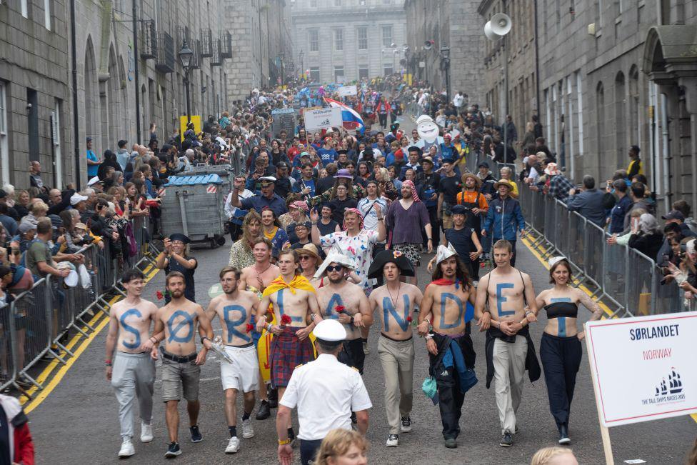 Parade, with tall ships crew members with word 'Sorlandet - one of the ship names - painted on their chest.
