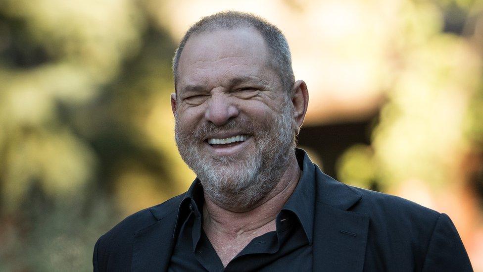 Harvey Weinstein, dressed in a dark jacket and shirt, is pictured smiling at the camera in a sunny outdoor setting in 2017