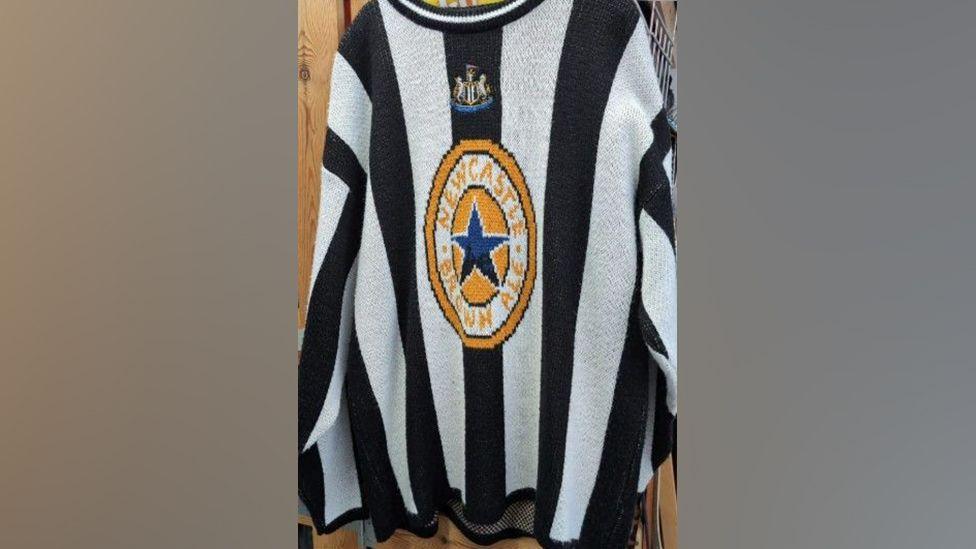 A Newcastle knitted jumper which is black and white with the Newcastle Brown Ale logo on the front 