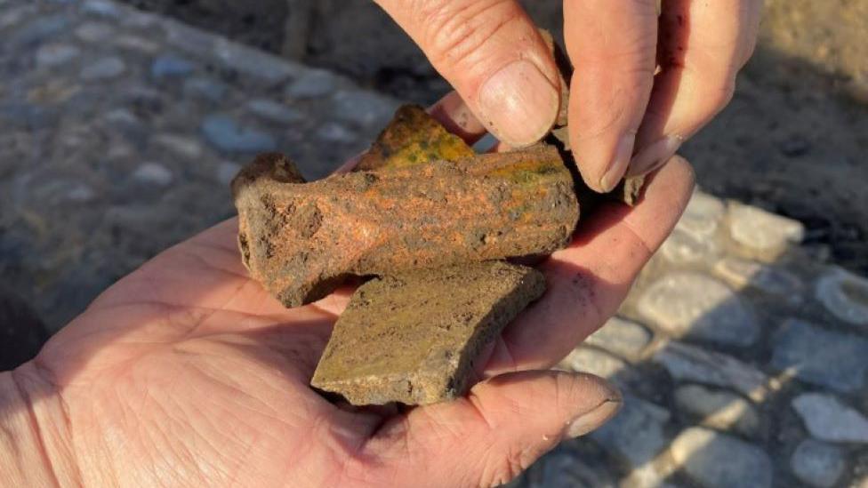 A person holds fragments of medieval artefacts in their hands above a cobbled street.