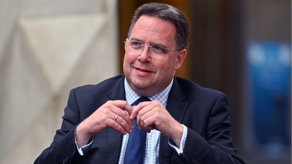 A man with dark hair and glasses in a dark suit sitting in the Scottish Parliament