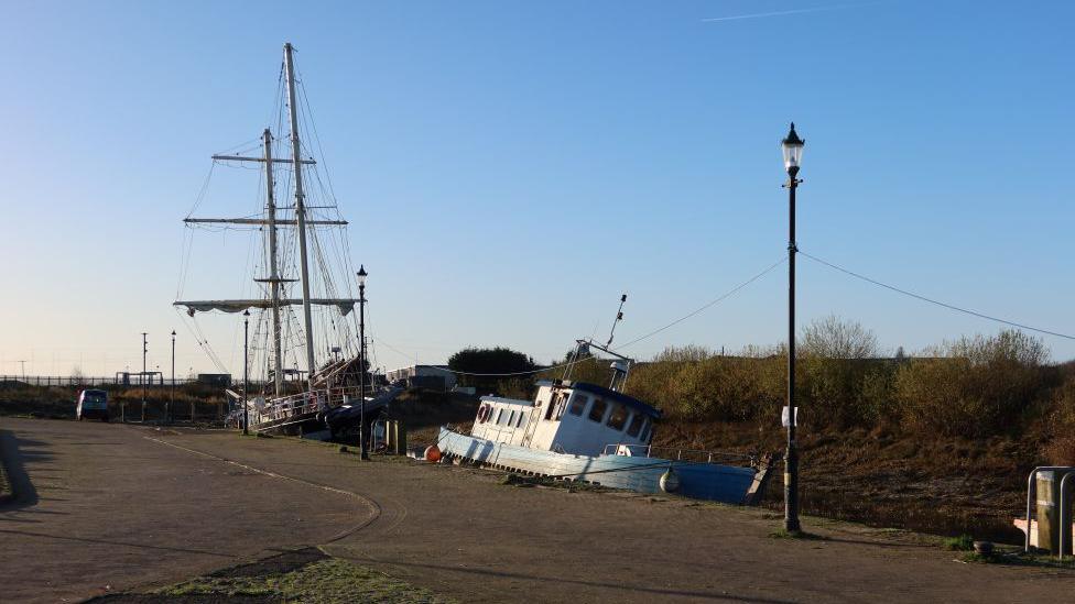 Two boats by the quayside. One is upright but a second - in the foreground - is tilting to the right. 