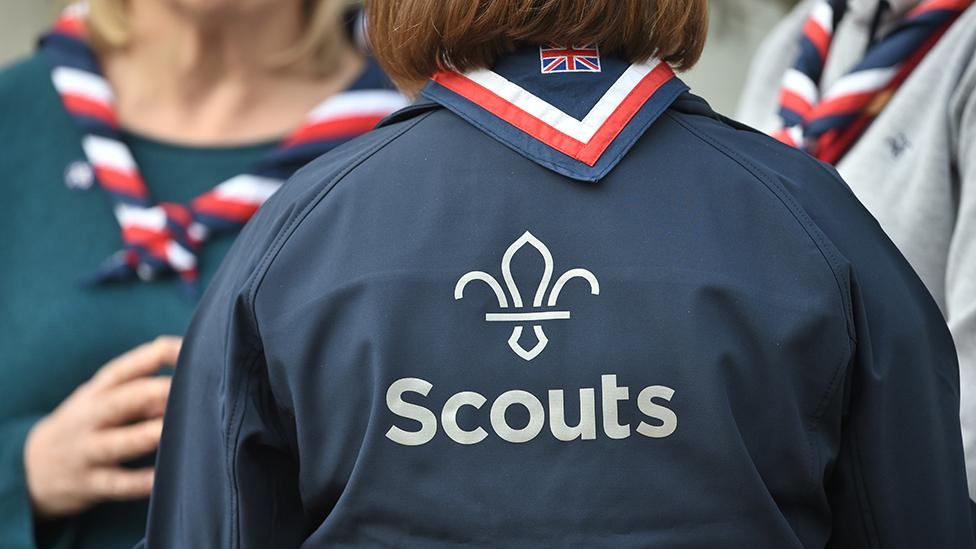 The Scouts logo is seen on the back of an anonymous Scout leader's shirt, with other anonymous Scouts in the background, taken at the Scouts' Headquarters in Gilwell Park, Essex in March 2019.