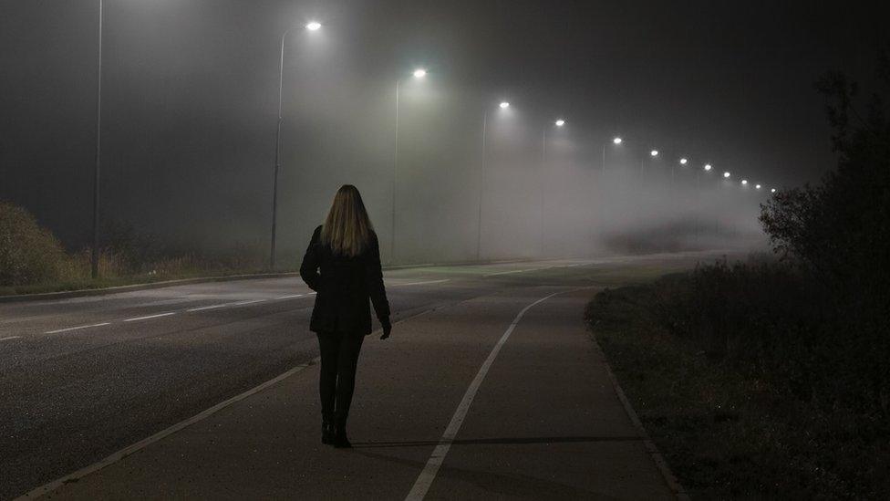 Woman walking along street lit by street lights