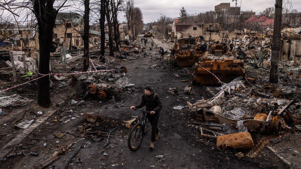 A man pushes his bike through debris and destroyed Russian military vehicles on a street on April 06, 2022 in Bucha, Ukraine.