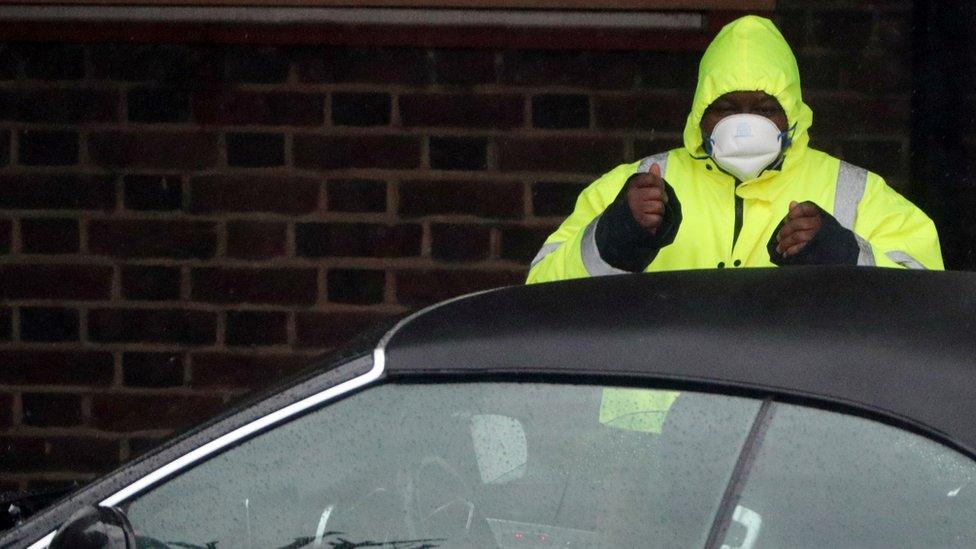 A security guard wears a surgical mask as he assists a car at a Coronavirus drive-through test centre at Parson"s Green Medical Centre in London