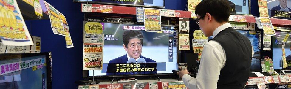 An employee in Japan at an electronics retail store checks televisions displaying news coverage of Japanese Prime Minister Shinzo Abe's visit to Hawaii - 28 December 2016