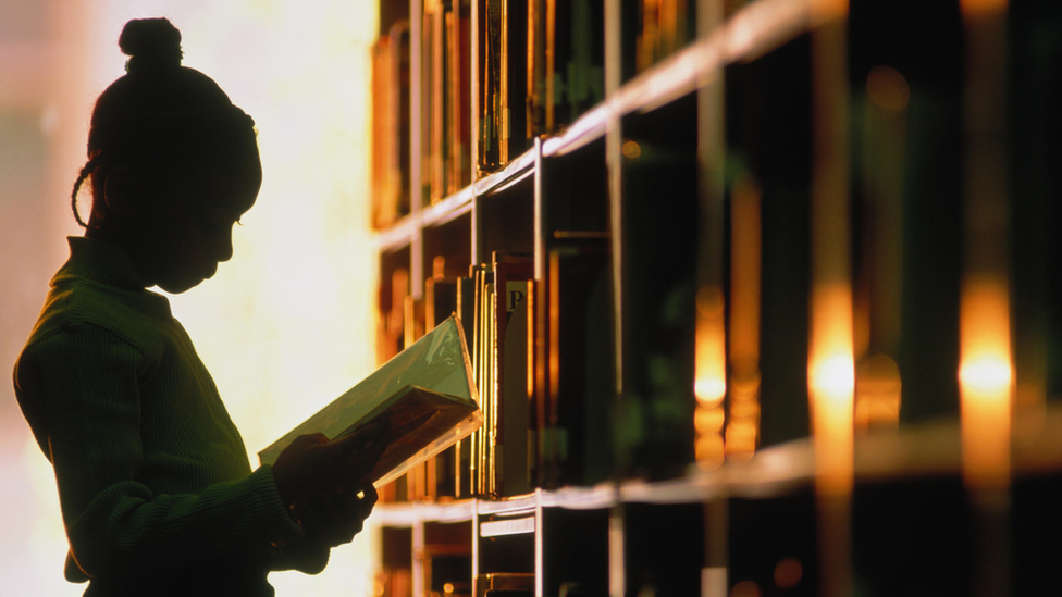 A young girl picks out a book from a bookshelf