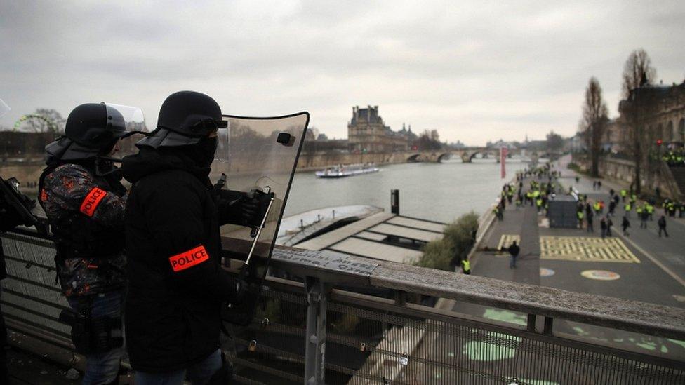 French riot police stand guard on a bridge over the Seine river overlooking protesters below as clashes erupt during a "yellow vests" protest in Paris, on 5 January 2019