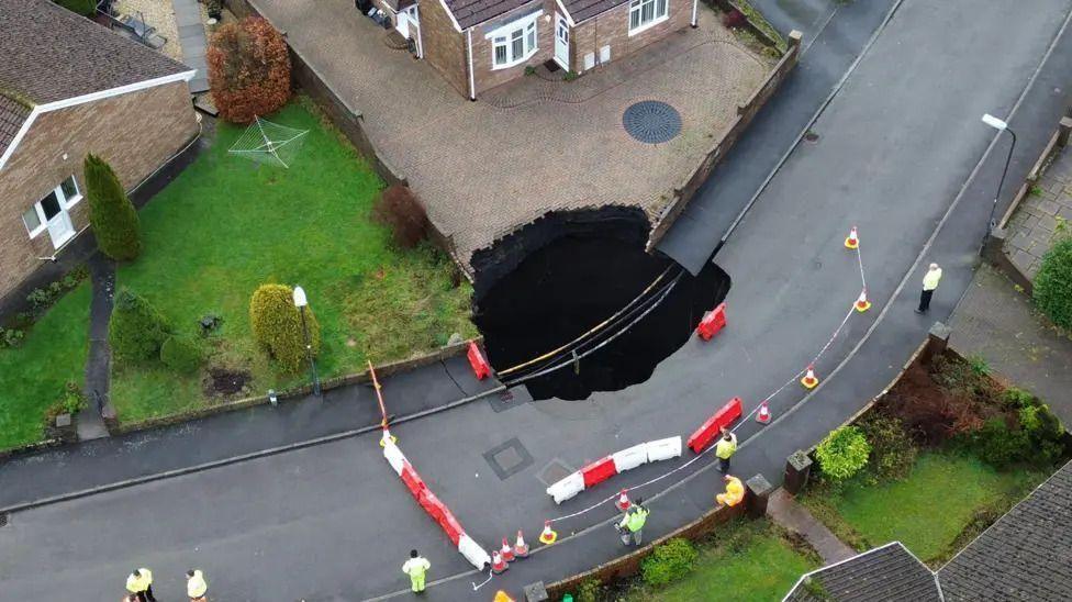 An aerial view of the street with the huge sinkhole and barriers and emergency services surrounding it