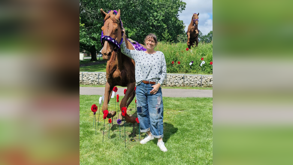 Gaynor White - wearing jeans and a blue and white top - and one of the horse statues with the charity's work before two of the three were stolen