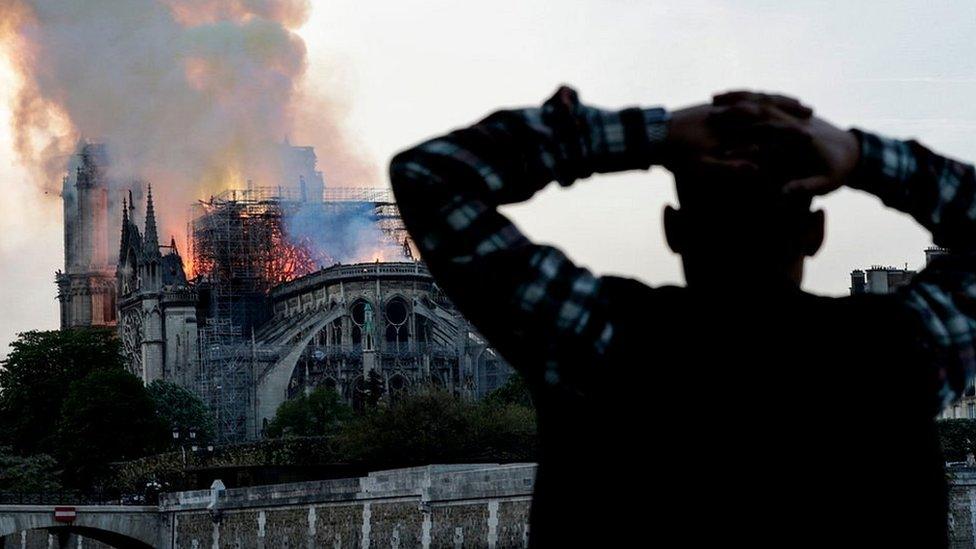 A man watches the landmark Notre-Dame Cathedral burn, engulfed in flames, in central Paris on April 15, 2019