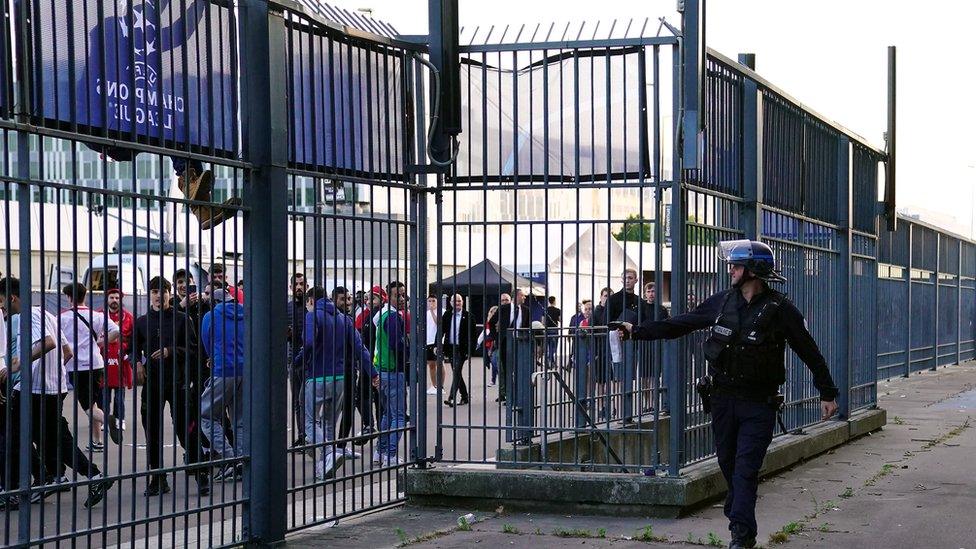 A policeman is seen pointing what appears to be a tear gas cannister at fans outside the Stade de France on Saturday