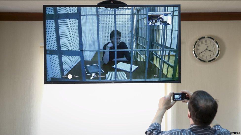 A man takes a picture of Ukrainian military pilot Nadia Savchenko as she is seen during a video link on a screen installed inside a court building during a hearing in Moscow, Russia (1 July 2015)