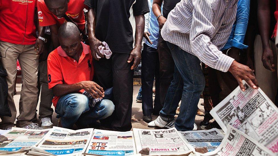 People gather in Brazzaville around a newspaper vendor where copies of Congolese daily newspapers are displayed